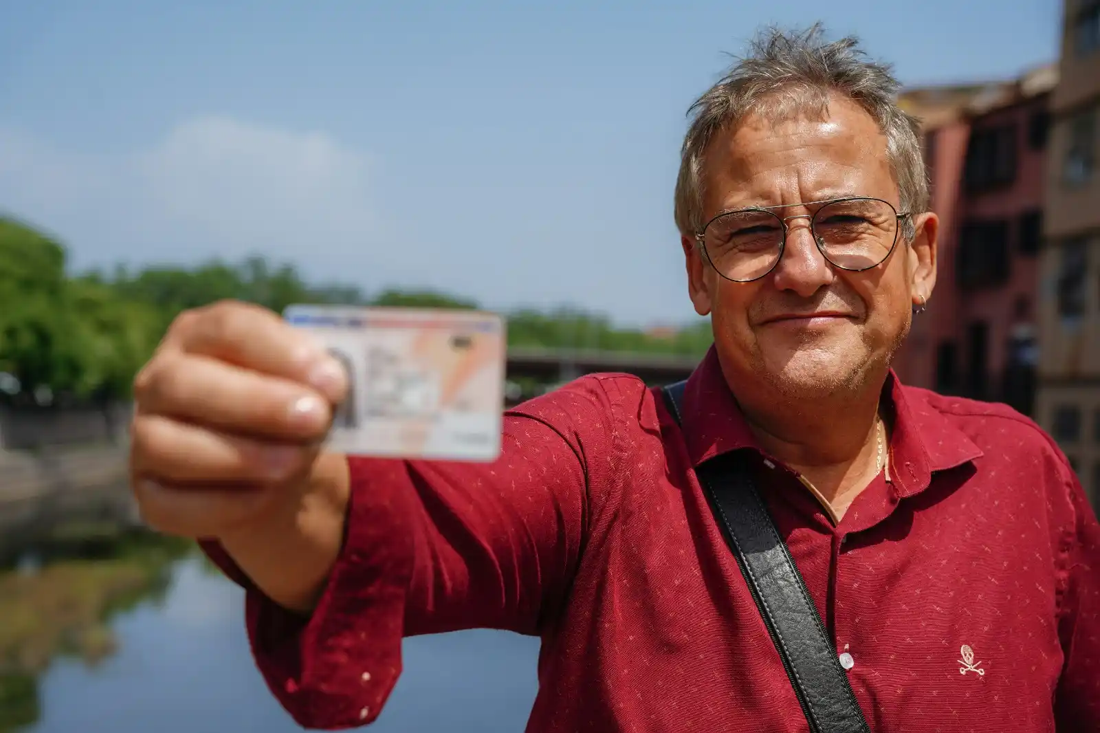 Man in his 60s wearing a red shirt and holding a TIE card (Spanish Foreigner Identity Card)